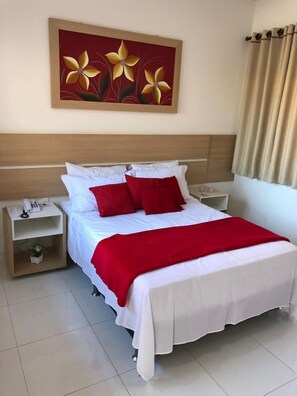 Un lit bien fait, avec une literie blanche et rouge, une table de chevet sur laquelle se trouve un téléphone, et une œuvre d’art représentant des fleurs, accrochée au mur.