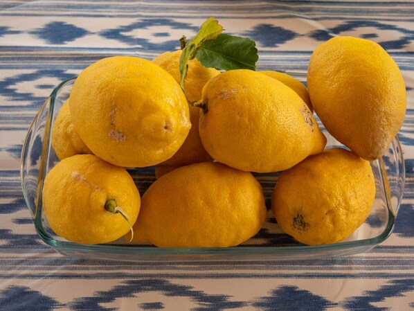 A glass dish containing several lemons on a patterned tablecloth.