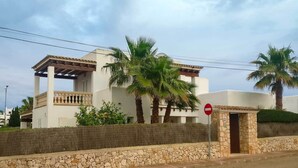 A two-story building with a balcony, palm trees, and a stone wall. - Spacious Villa in Cala D'or Marina  (Cala D'or)