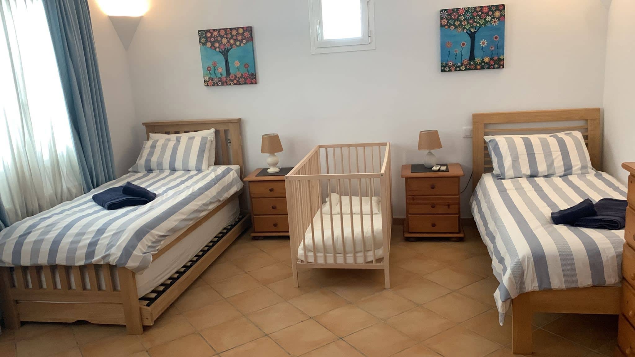 Ein Zimmer mit zwei Betten, einem Babybett und zwei Nachttischen.