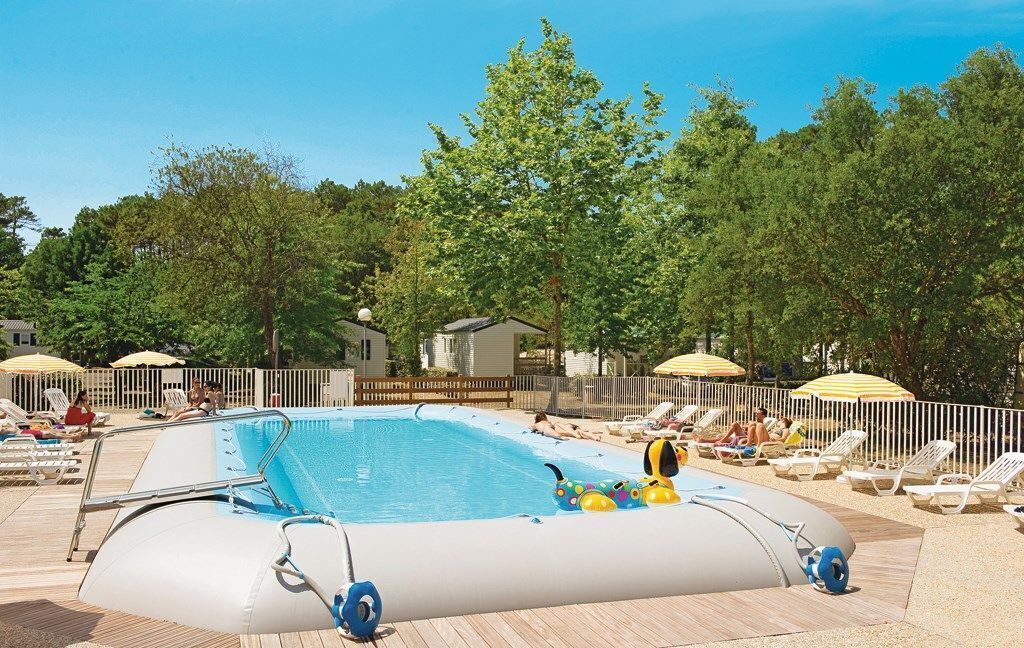 A swimming pool with lounge chairs and umbrellas, surrounded by trees and a wooden deck.