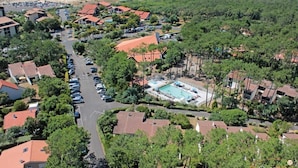 Vista aérea de un complejo turístico costero con varias edificaciones, un estacionamiento y una piscina.