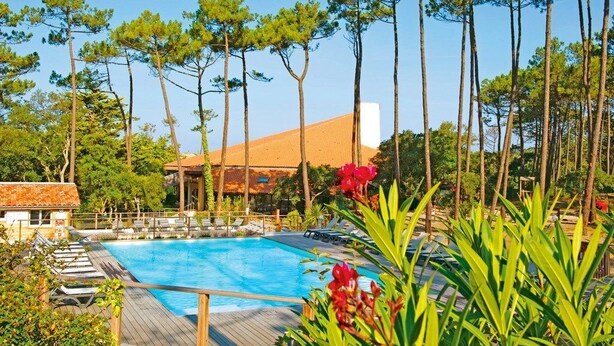 Un área de piscina con sillas de descanso, una terraza de madera y  árboles altos.