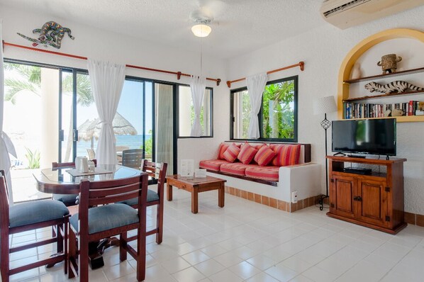 Sala de estar com sofá, TV e área de jantar com cadeiras e mesa.