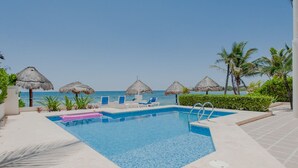 A pool area with clear blue water, lounge chairs, and thatched umbrellas.