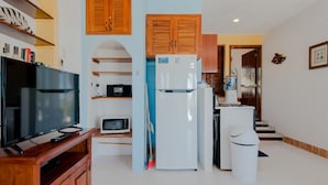 A compact kitchen with a refrigerator, microwave, and a television on a wooden stand.