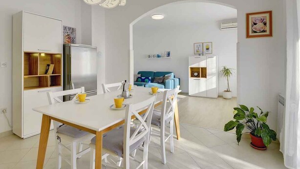 A modern kitchen with white cabinetry, a dining table with chairs, a refrigerator, and a hanging light fixture.