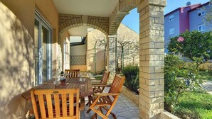 An outdoor patio with a wooden table and chairs, stone arches, and a view of a building in the background.