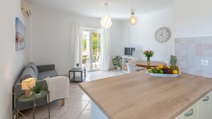 Et moderne køkken med træbordplade, spiseplads med bord og stole, en sofa og et stort vindue med gardiner.
