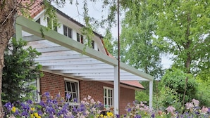 A garden with a variety of flowers in front of a house with a white porch and a brick facade.