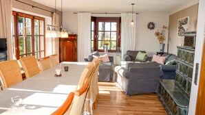 A spacious living room with a dining area, wooden flooring, and large windows.