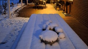A covered patio area with a snow-covered ground, a table and chairs, and a brick building in the background.