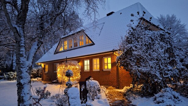A snow-covered house with a brick exterior, a visible front porch, and a pathway leading to the entrance.