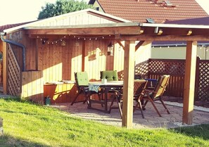 A wooden outdoor patio with a table and chairs, surrounded by a wooden fence and string lights.