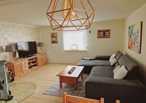 A living room with a TV, wooden cabinet, grey sofa, and a geometric pendant light.