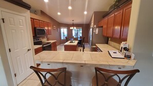A kitchen with wooden cabinets, a microwave, an oven, a refrigerator, and a dining area with two chairs. - Lake Havasu Pool Garage/Boat Parking 5Min Riviera Marina London Bridge & DT (Lake Havasu City)