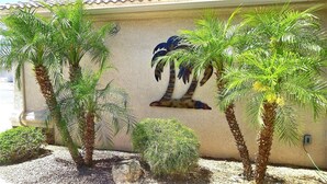 A building exterior with a mural of a palm tree, surrounded by live palm trees and shrubs. - Lake Havasu Pool Garage/Boat Parking 5Min Riviera Marina London Bridge & DT (Lake Havasu City)