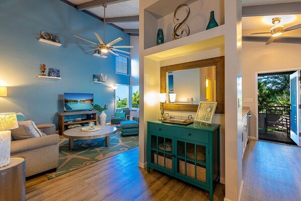 Una sala de estar moderna con una pared azul, un ventilador de techo, un espejo grande y un comedor con mesa y sillas.