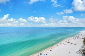 Een strand met helder turquoise water, een zandstrand en enkele parasols.