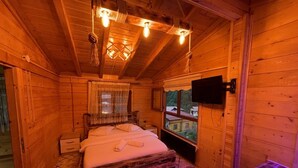 Un dormitori de cabana de fusta amb un llit, una finestra que ofereix una vista, un televisor penjat i una banyera.