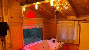 Una cabana de fusta amb una banyera gran, parets de fusta i una finestra amb vista als arbres.