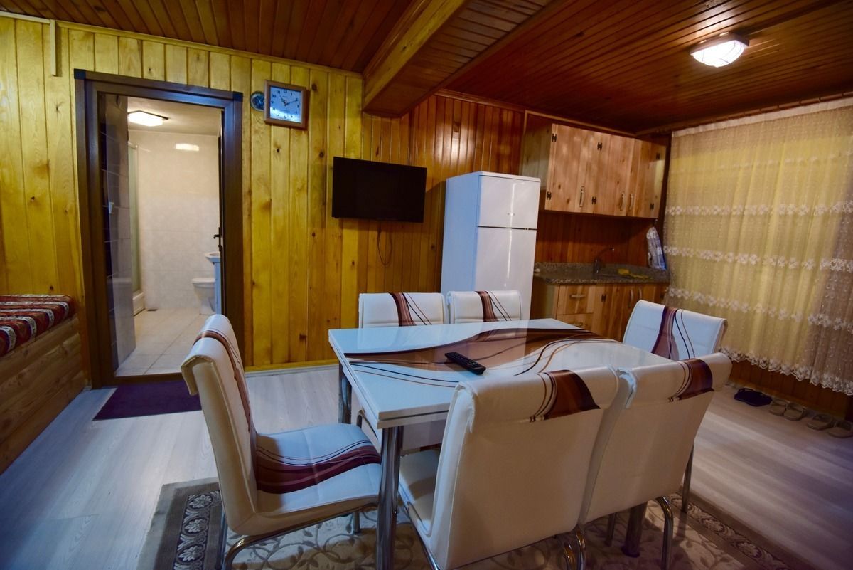 A wooden cabin interior with a dining table, chairs, a television, and a kitchen area.