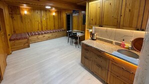 Interior d'una cabana de fusta amb una cuina, una taula de dinar i una banca.