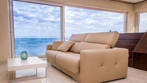En beige soffa med utsikt över havet genom stora fönster.
