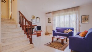 Ein Wohnzimmer mit Treppe, einer Couch, einem Couchtisch und einem Fernseher.