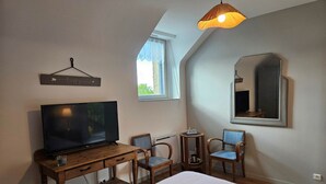 A bedroom with a bed, a TV on a wooden desk, two chairs, a small table, a hanging light, a window, and a mirror on the wall. - Groix Island Bed and Breakfast (BELZ)