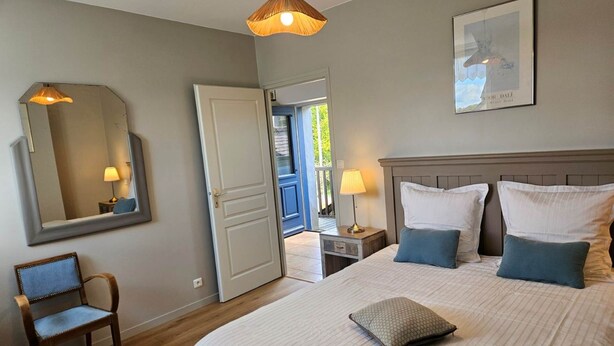 A bedroom with a bed, bedside lamps, a chair, a mirror, and a door leading to a balcony. - Groix Island Bed and Breakfast (BELZ)