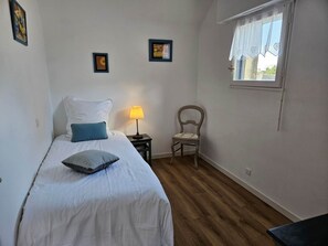 A bedroom with a bed, a nightstand, a chair, a window with curtains, and wall art.