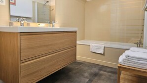 A modern bathroom with a wooden vanity, a bathtub, and a shower area. - Groix Island Bed and Breakfast (BELZ)