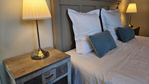 A neatly made bed with white and blue pillows, a wooden nightstand with a lamp, and a matching lamp on the opposite side. - Groix Island Bed and Breakfast (BELZ)