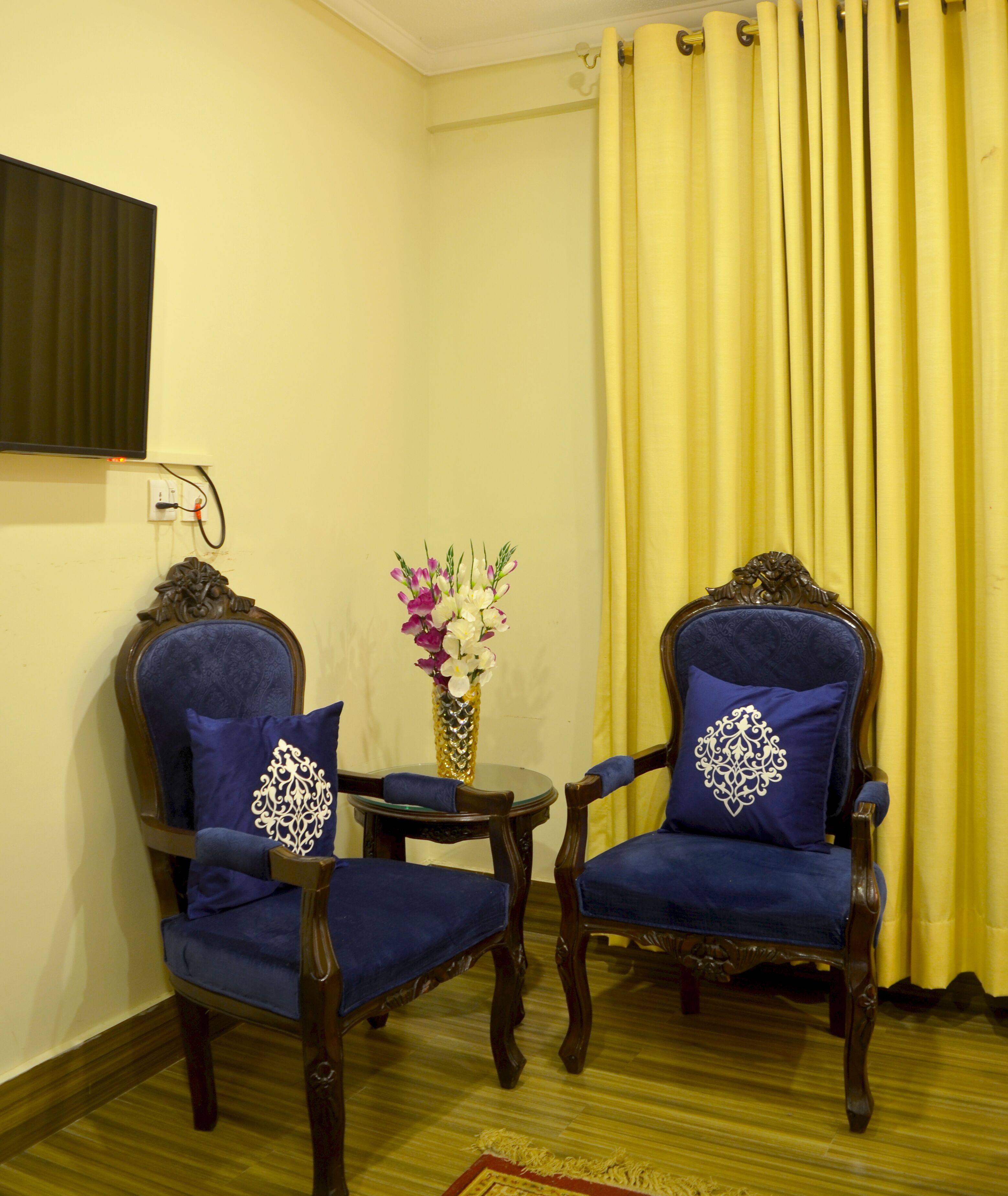 Deux fauteuils bleus, recouverts d’un tissu décoratif, agrémentés de coussins, une petite table ronde et un vase rempli de fleurs.