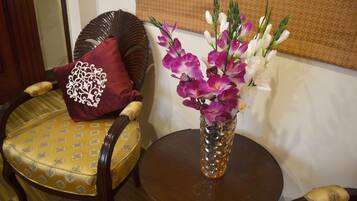 Una habitación con una mesa redonda de madera, una silla amarilla estampada y un jarrón con flores moradas y blancas.