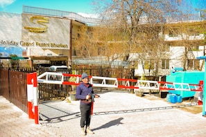 Entrada com portão e cerca de metal para o Holiday Grand Resort Bhuban, com barreira vermelha e branca.