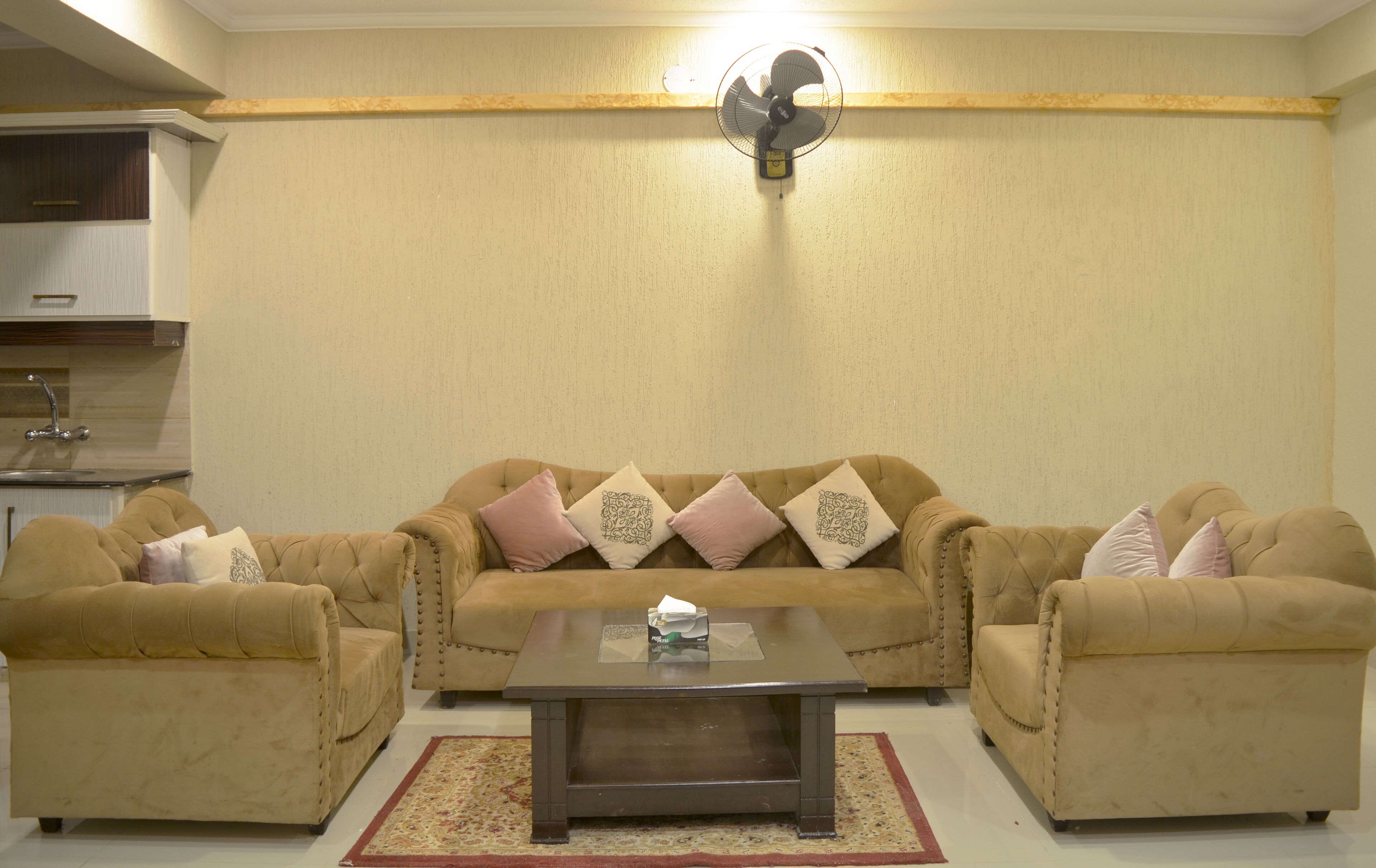 A living room with a beige sofa set, a coffee table, and a wall-mounted fan.