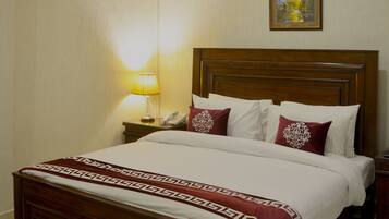 Una habitación de hotel con una cama de madera, una lámpara de noche, un aire acondicionado y un cuadro en la pared.