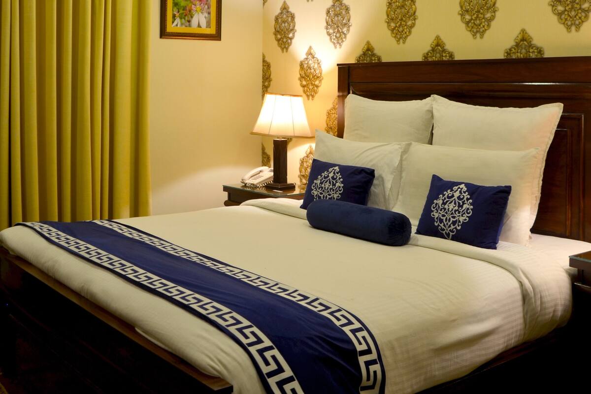 Une chambre d’hôtel comprenant un lit, une table de chevet, une lampe, un appareil de climatisation et un papier peint à motifs.
