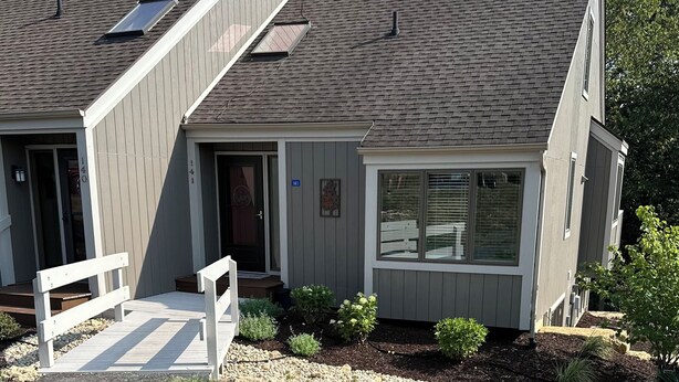 A two-story house with a sloped roof, a front porch with a bench, and a small garden area with plants and gravel. - 2BR 2BA + 3rd BR loft cozy end unit lakefront townhome comfortably sleeps 6! (Galena)
