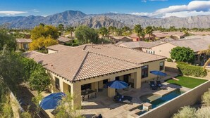 A residential area with houses featuring red-tiled roofs, a swimming pool, and a view of mountains in the background.