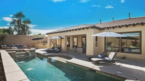 A pool area with lounge chairs and umbrellas, a tiled roof, and a brick wall.