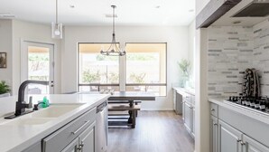 A modern kitchen with a large island, white cabinetry, and a view to the outdoors.