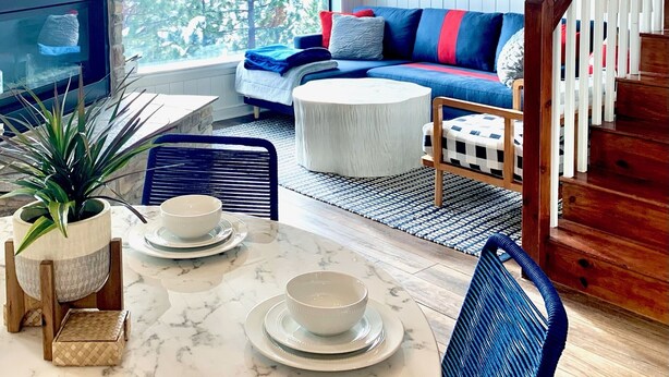 A cozy living room with a fireplace, a sofa, a coffee table, and a dining area with a table set for two.