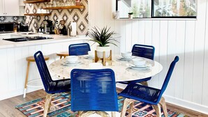 A dining area with a round table, blue chairs, a chandelier, and a patterned rug.