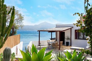 A patio with a table and chairs, overlooking a body of water and mountains. - Skinopi Fisherman's house (Schinopi)