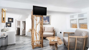 Ein modernes Wohnzimmer mit Fernseher auf einem Holzboden, einer Couch, einem Couchtisch und einem Korbstuhl.