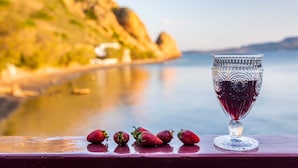 Ein Glas Rotwein und Erdbeeren auf einer Holztischplatte, im Hintergrund Meerblick.