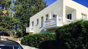 A two-story building with a balcony, a car parked in front, and a hedge with red flowers. - Apartment in Kato Paphos (Phafos)
